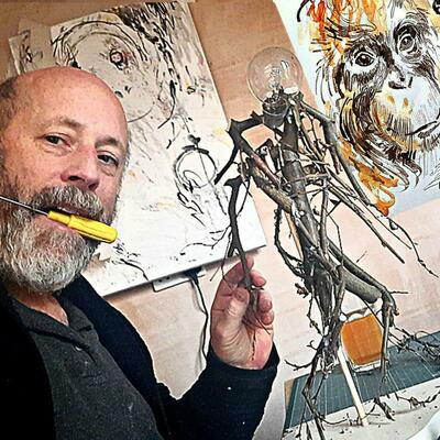 Working in my studio on a mixed media sculpture of running figure (twigs and light bulbs); in the background are 2 of my paintings of orangutans.