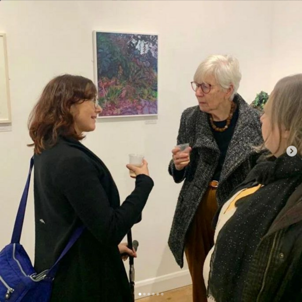 Artist talking to 2 visitors, standing in front of her artwork.