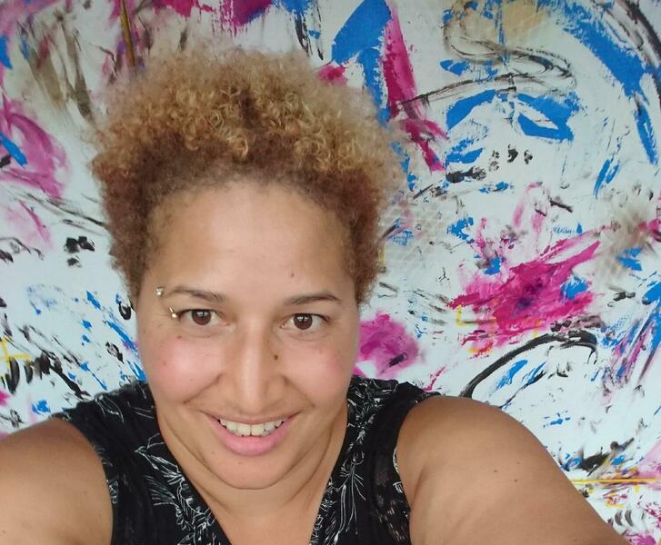 selfie image of IJE smiling, in front of a white, pink, blue and gold painting