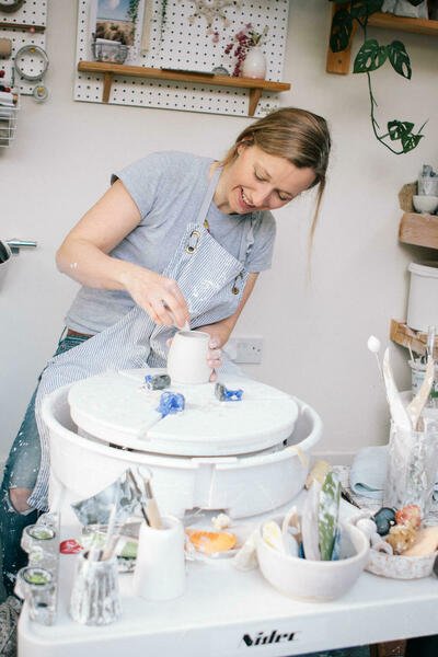 Ceramic artist, Katie Robbins, working at her wheel, turning a porcelain pot.