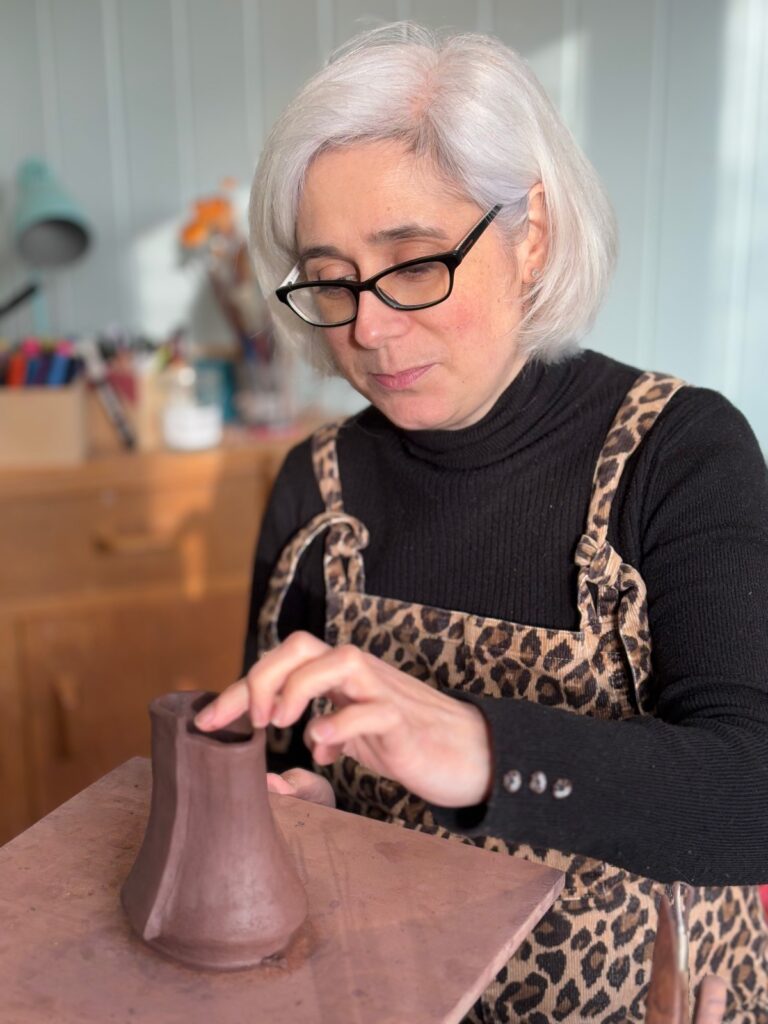 Katherine Taylor ceramicist is sitting hand building a small vessel with black stoneware clay