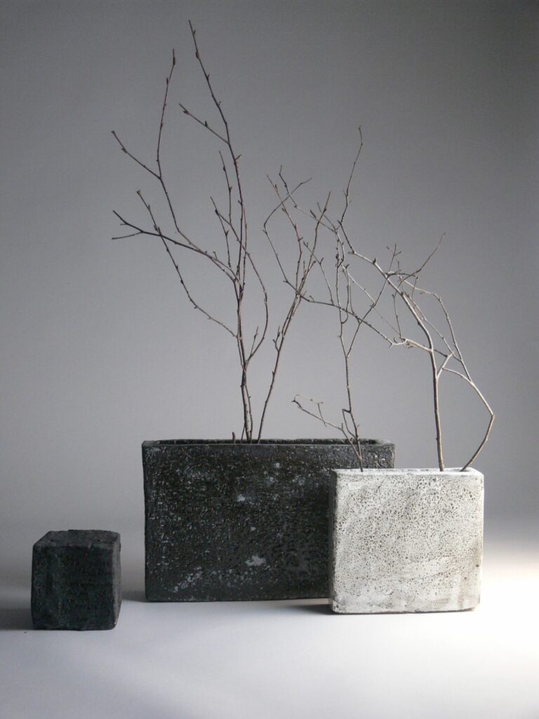 Two Ikebana inspired rectangular vases, one black, one white and a square black ceramic block