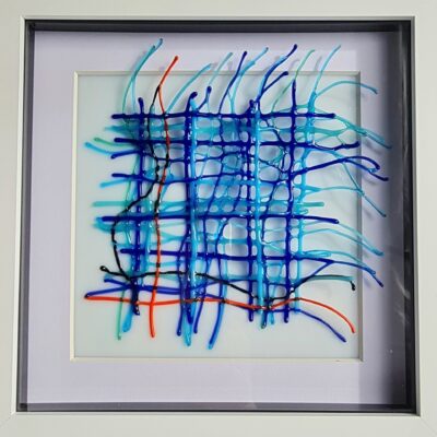  A square frame holding a woven fused glass design.  The thin woven threads are made up of wavy strands of blue glass woven together to form a pattern which flows out of the frame.  One strand of red glass flows across the bottom of the design.